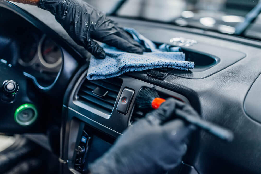close up image of a cleaner wearing black gloves cleaning the air vents of a car interior