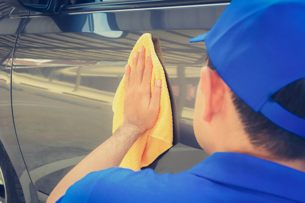 view from behind the head of a worker wiping down the side of a car with a cloth