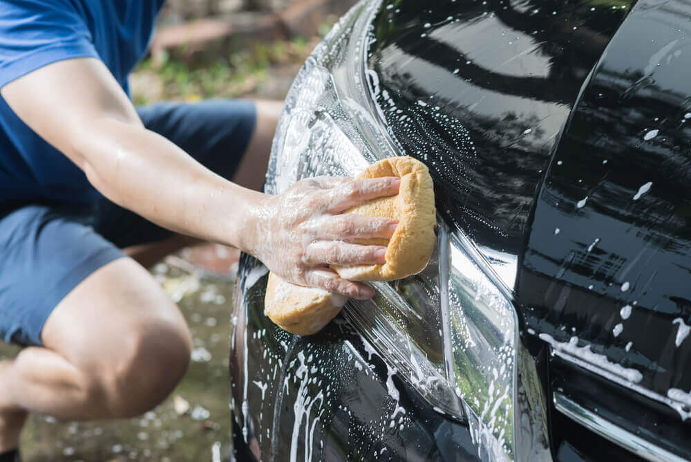 outside image of a cleaner washing the headlight of a car with a sponge and soapy water