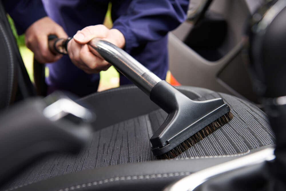 image of the seat of a car with somebody vacuuming the seat