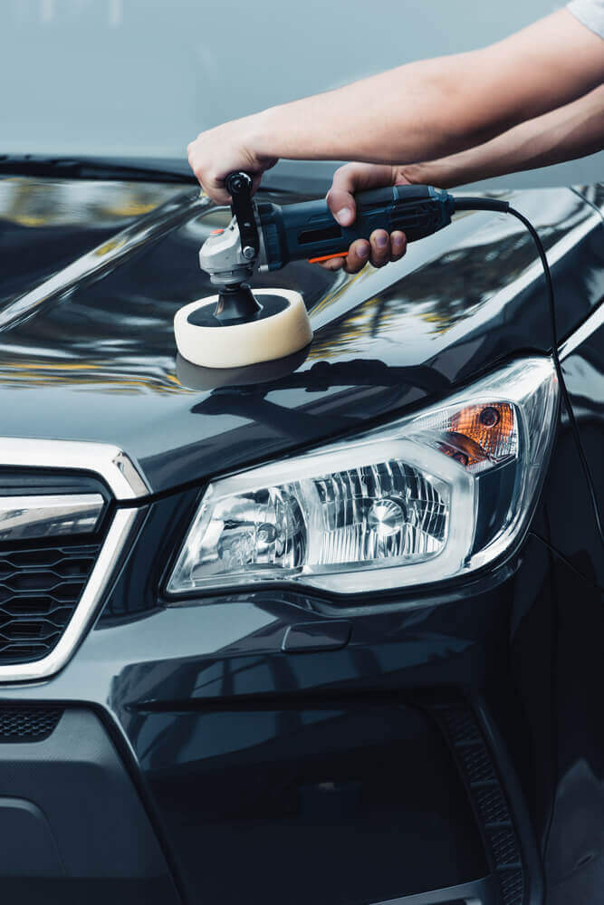 front view of a cleaner using a buffing machine on the bonnet of a black car