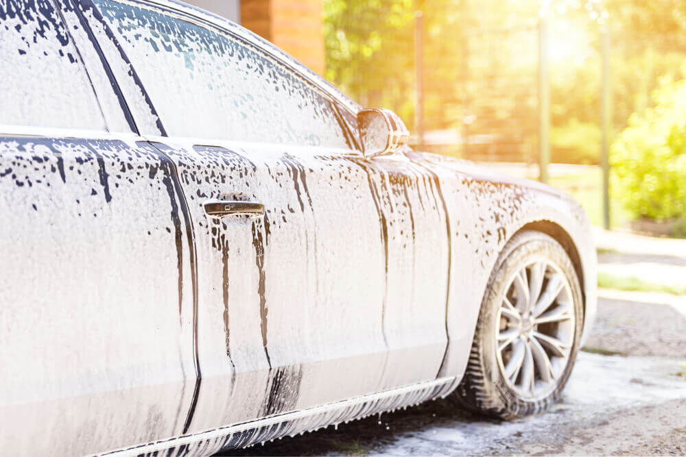 side image of a car covered in white bubbles being washed