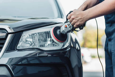 front shot of a cleaner buffing the headlight of a car with protective tape surrounding the headlight