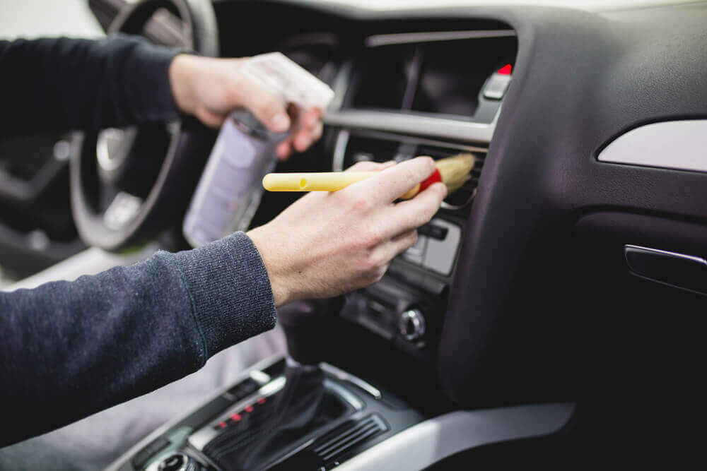 close up image of a cleaner using a brush to clean the dash of a car