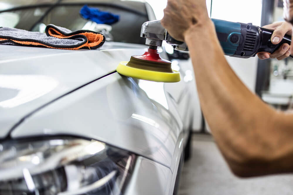 shot of a cleaner buffing the top of a cars front panel with a buffing machine