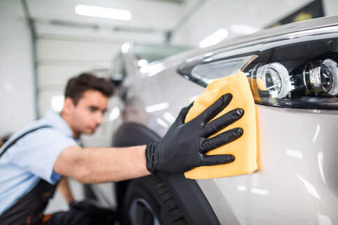 image of a worker wiping down the side of a clean car with a yellow cloth